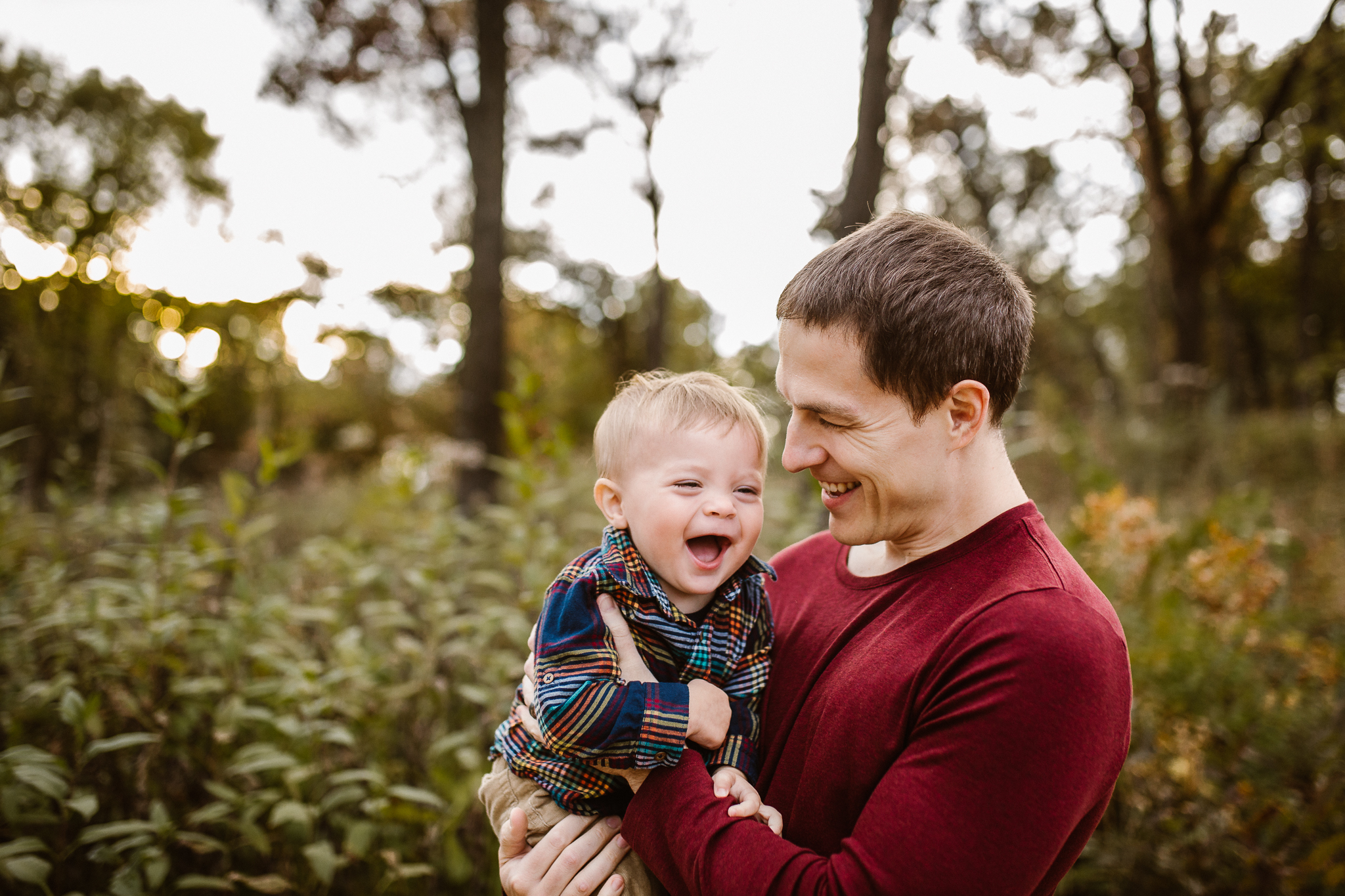 One year old boy laughing in his father's arms outside.